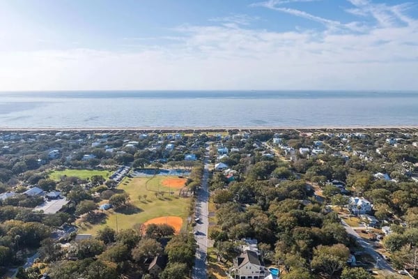 Aerial view of coastal residential neighborhood with sports fields, tree-lined streets, and bay water beyond